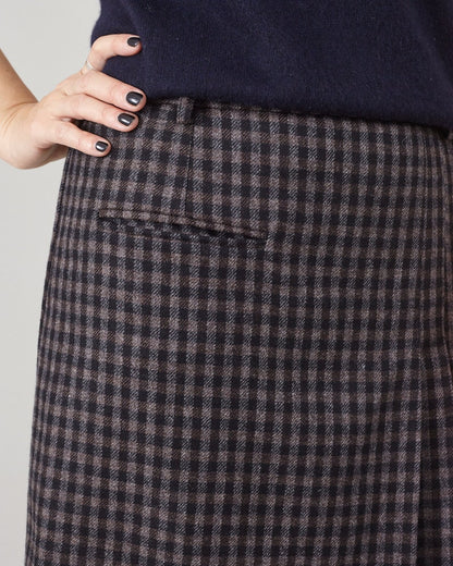 Close-up of a person wearing a dark blue sweater and brown checkered skirt on a light gray background