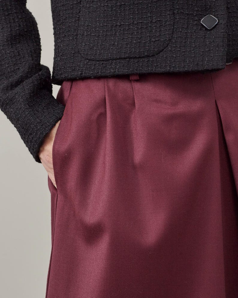 Close-up of maroon pleated skirt with a textured dark jacket on a neutral background