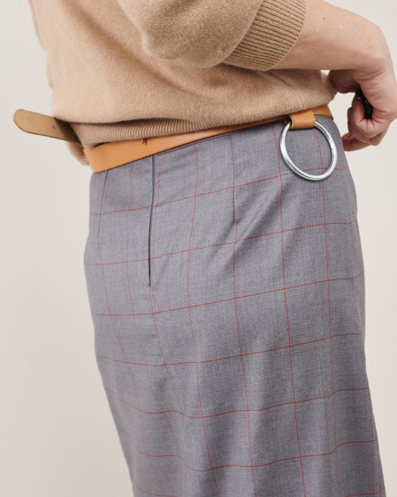 Person wearing a beige sweater and gray plaid skirt with a belt.