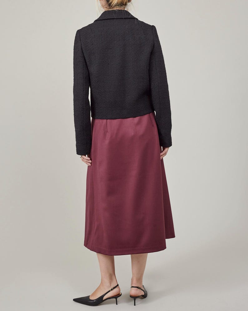Person wearing a black jacket and burgundy skirt on a plain background