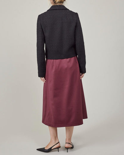 Person wearing a black jacket and burgundy skirt on a plain background