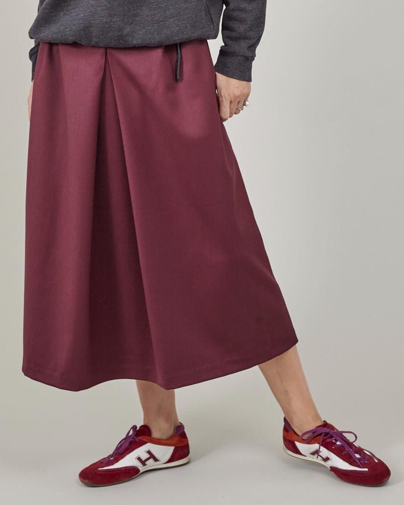Person wearing a burgundy skirt and red and white shoes on a plain background