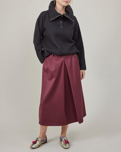 Person wearing a dark sweater and burgundy skirt on a plain background