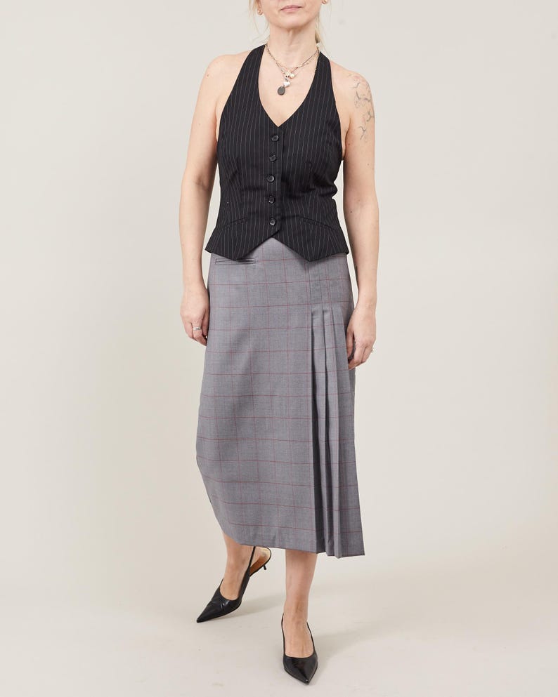 Person wearing a black halter sweater vest and gray plaid skirt on a beige background