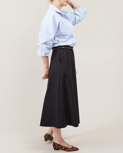 Person wearing a light blue shirt, black skirt and animal print shoes on a plain background