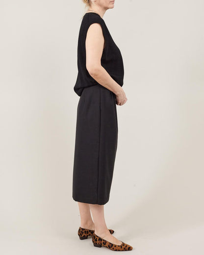 Person wearing a black sleeveless top and skirt set on a plain background