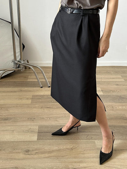 Person wearing a black midi skirt with a side slit and belt on a wooden floor.