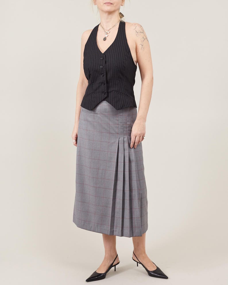 Person wearing a black sleeveless top and gray plaid skirt on a white background