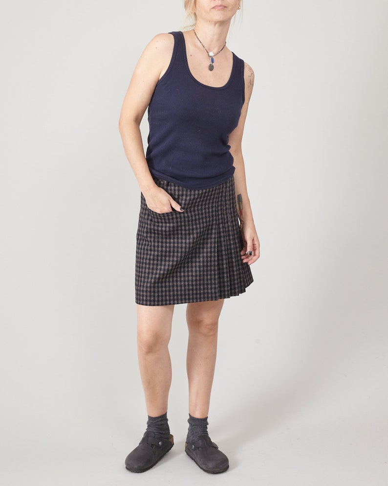 Person wearing a navy tank top and plaid skirt on a plain background