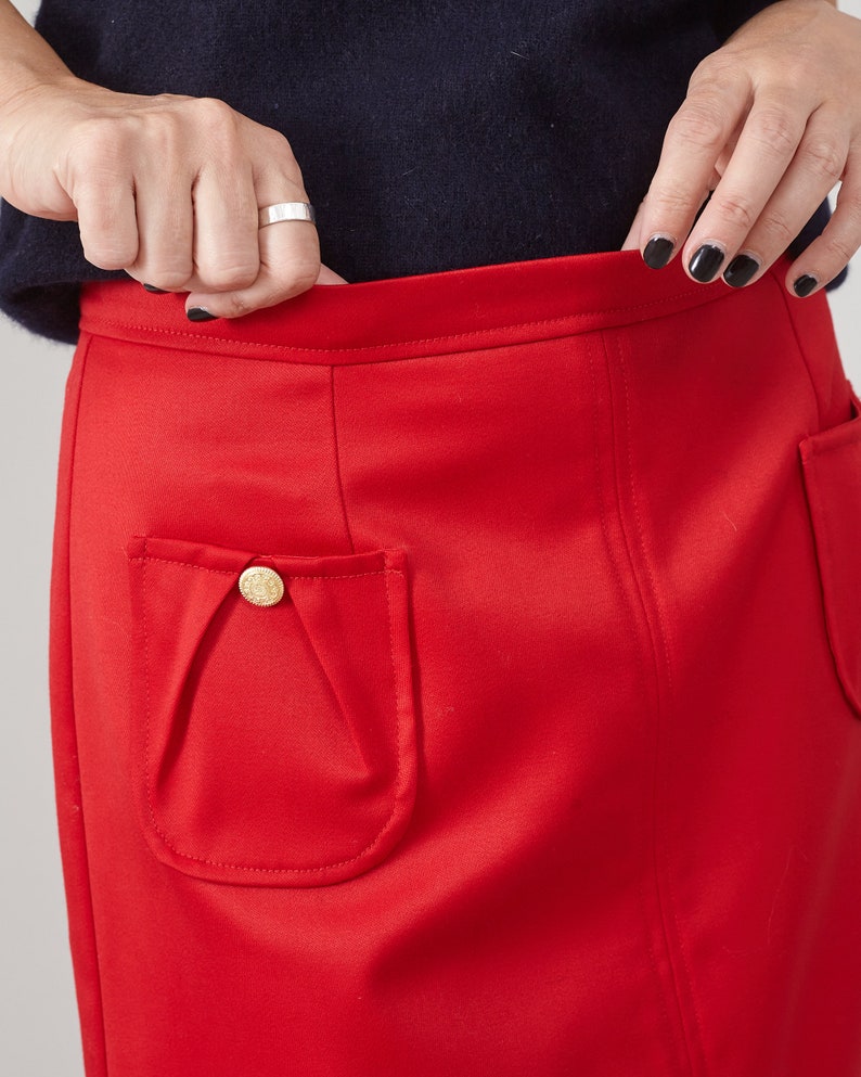 Red skirt with a gold button pocket worn by a person against a neutral background