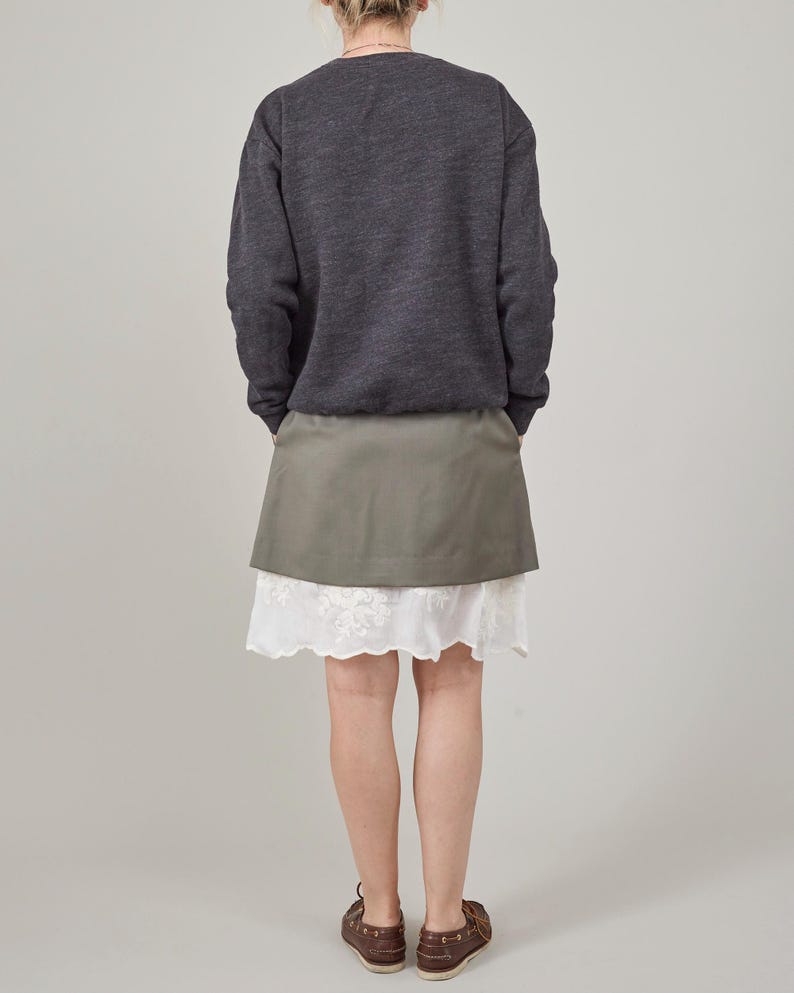 Person wearing a dark gray sweatshirt and light khaki skirt with a white lace hem