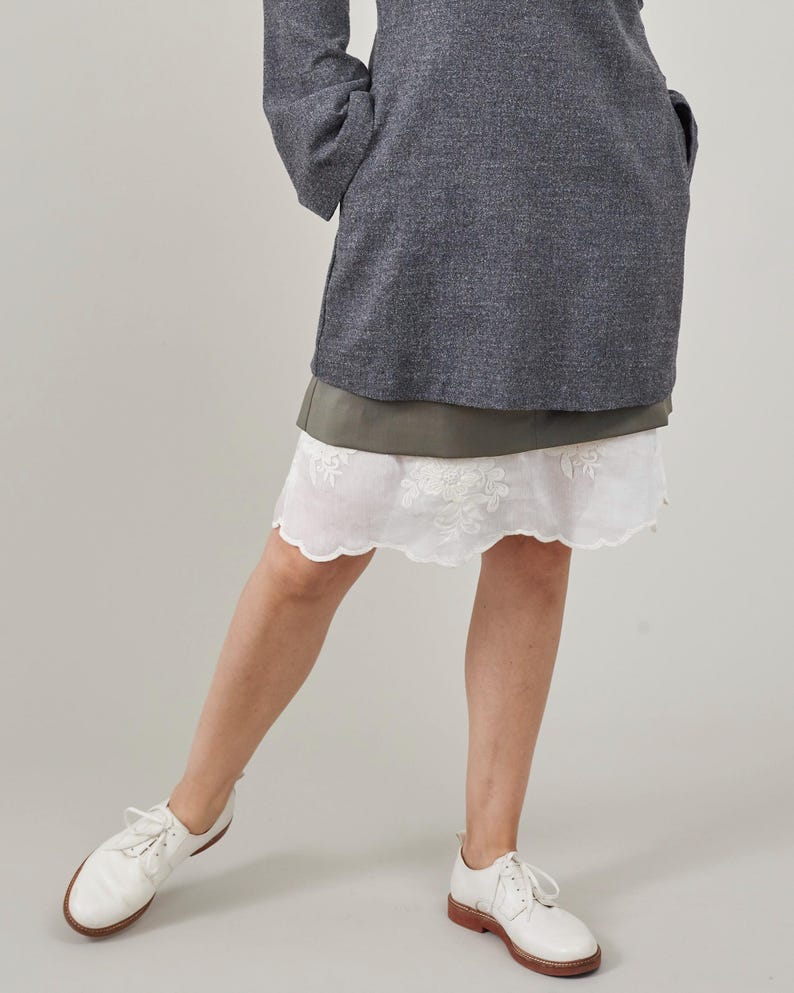 Person wearing a gray dress with a white lace trim skirt and white shoes on a plain background