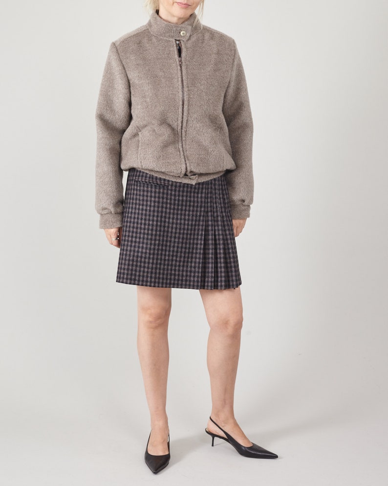 Person wearing a gray jacket and plaid skirt on a white background