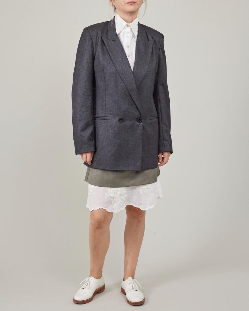 Person wearing a gray blazer over a white shirt and green skirt on a plain background