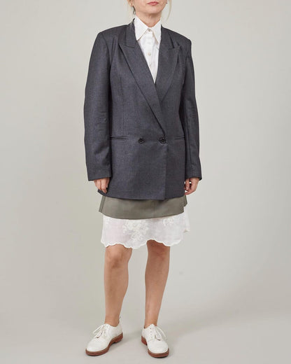 Person wearing a gray blazer over a white shirt and green skirt on a plain background