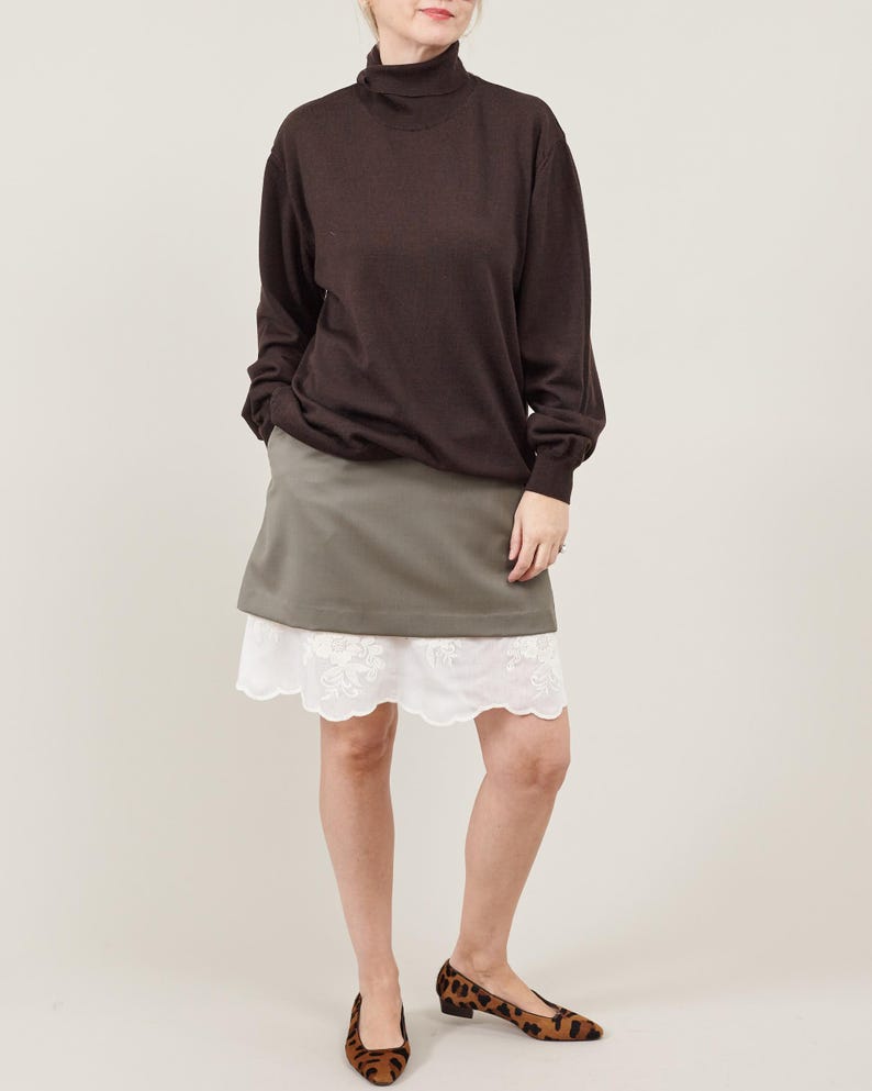 Person wearing a brown turtleneck, khaki wool mini skirt with white lace hem