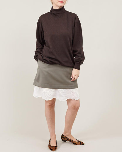 Person wearing a brown turtleneck, khaki wool mini skirt with white lace hem