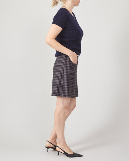 Woman wearing a navy top and plaid mii skirt on a plain background
