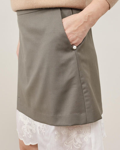 Person wearing a khaki skirt with a white lace under layer on a plain background