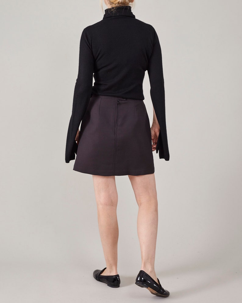 Person wearing a black turtleneck and dark brown skirt on a plain background