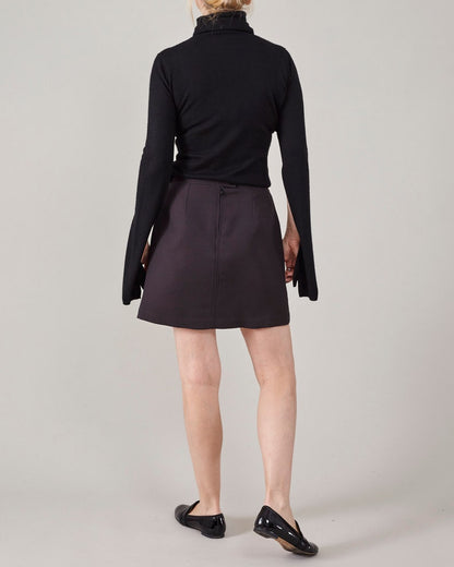 Person wearing a black turtleneck and dark brown skirt on a plain background