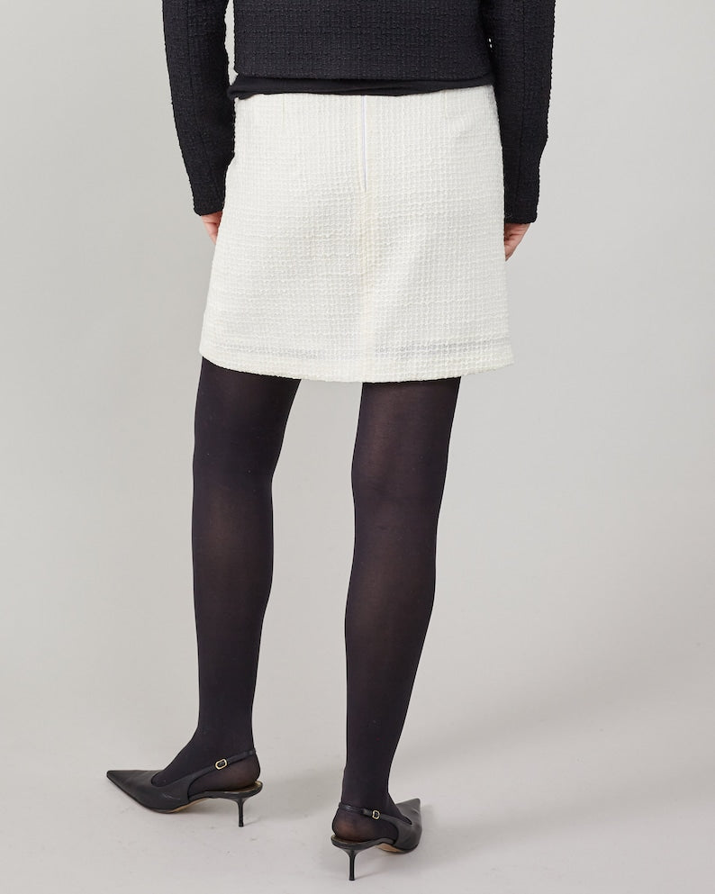 Person wearing a white skirt, black tights, and black shoes on a plain background