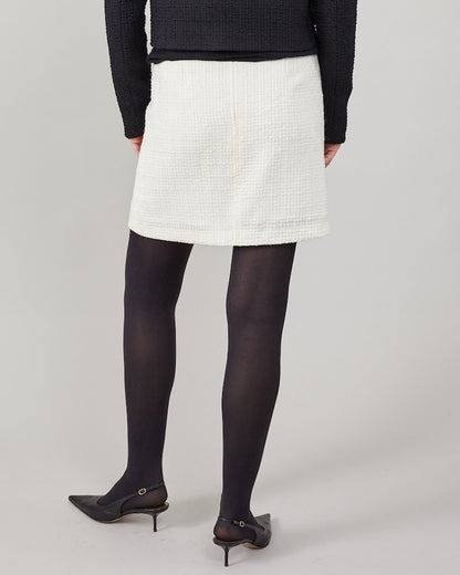 Person wearing a white skirt, black tights, and black shoes on a plain background