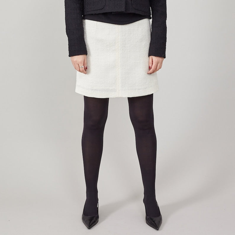 Person wearing a white skirt, black tights, and black shoes on a plain background