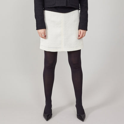 Person wearing a white skirt, black tights, and black shoes on a plain background