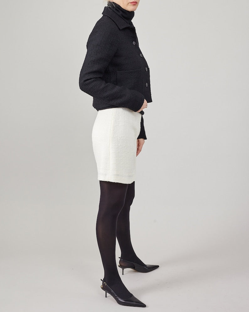 Person wearing a black jacket, white skirt, and black tights on a plain background