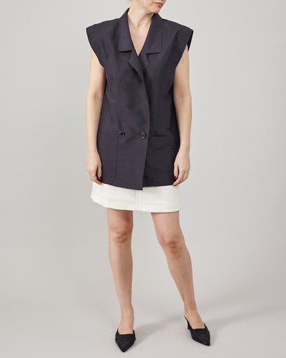 Person wearing a dark sleeveless jacket over a white skirt on a plain background