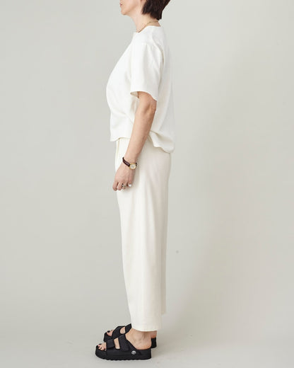 Side view of handmade ivory raw silk tapered trousers showing tapered silhouette and cropped length, styled with matching boxy top and black platform sandals, by Fine Thee