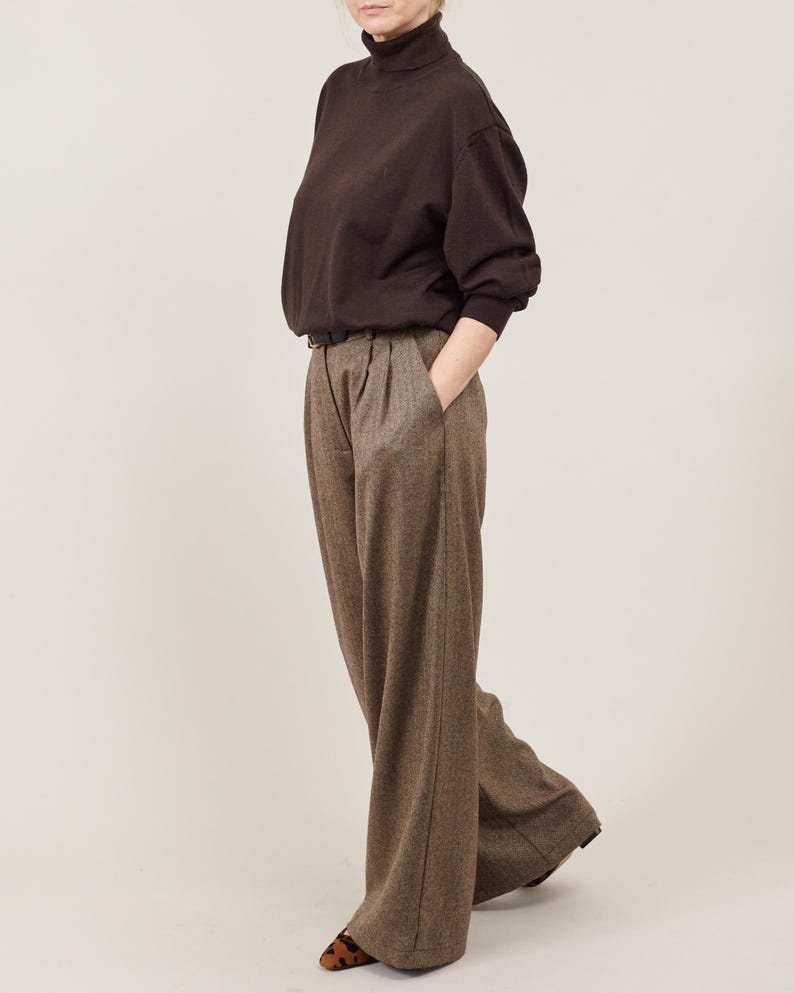 Person wearing a brown turtleneck and wide-leg pants and leopard print shoes on a plain background