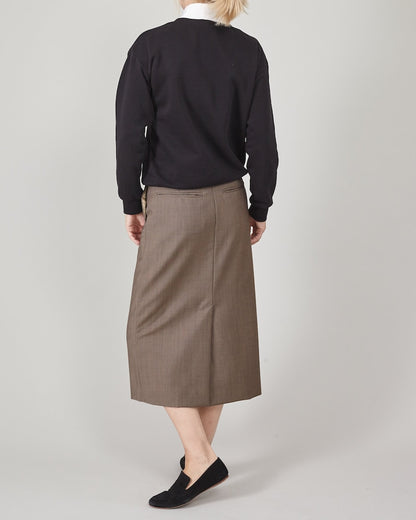 Person wearing a black sweatshirt, taupe midi skirt and black loafers on a plain background
