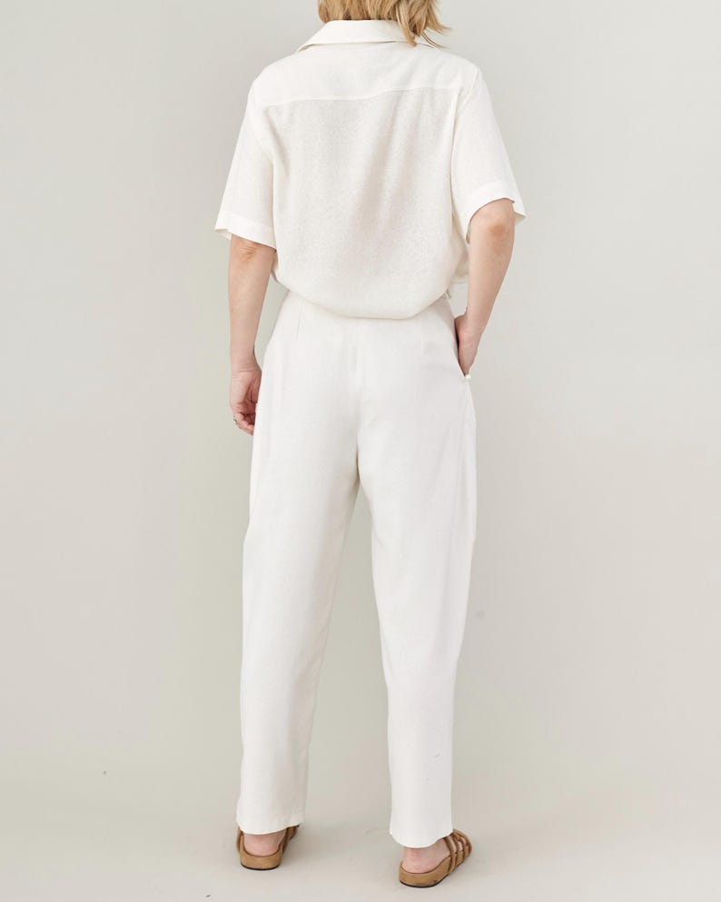 Person wearing an all white outfit with oversized short sleeve blouse and high waisted tapered pants on a plain background