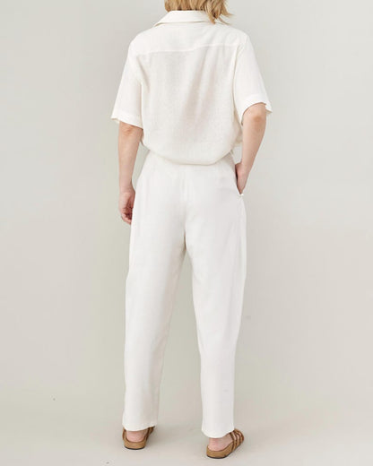 Person wearing an all white outfit with oversized short sleeve blouse and high waisted tapered pants on a plain background