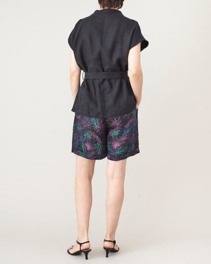 Person wearing a black outfit with colorful leaf patterned shorts on a white background