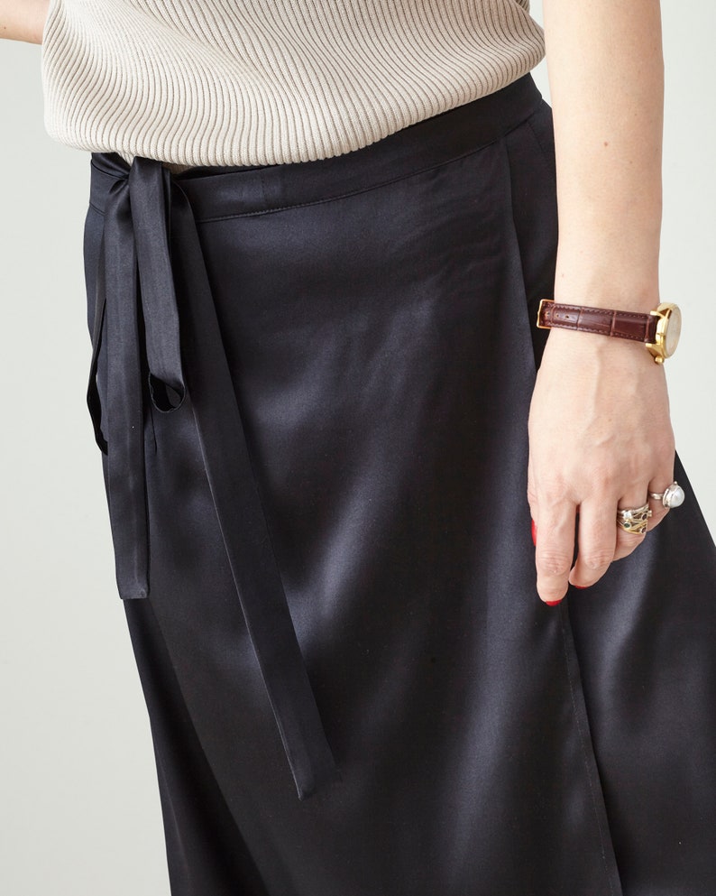 Person wearing black satin silk skirt with a tie detail on a plain background