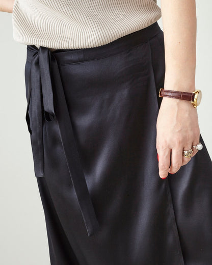 Person wearing black satin silk skirt with a tie detail on a plain background