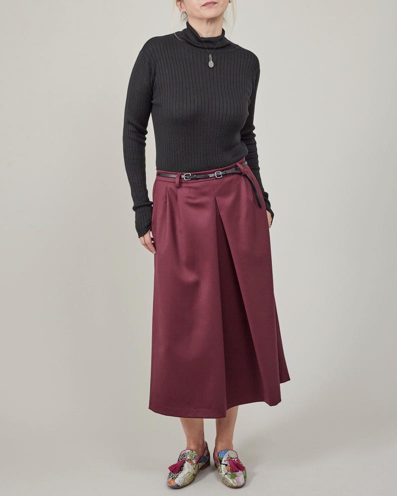 Person wearing a black ribbed sweater and burgundy skirt on a plain background