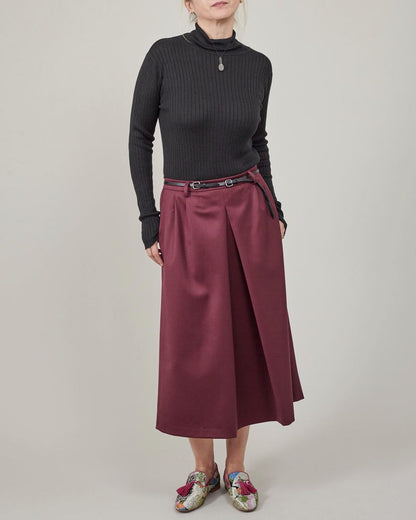Person wearing a black ribbed sweater and burgundy skirt on a plain background