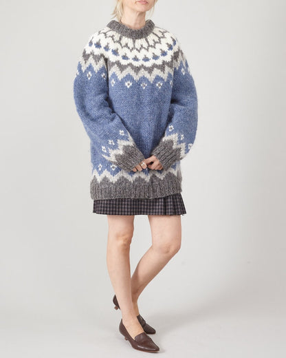 Person wearing a patterned sweater and plaid skirt on a white background