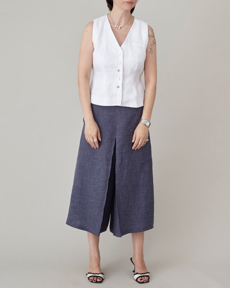Person wearing a white vest and blue wide-leg pants on a plain background