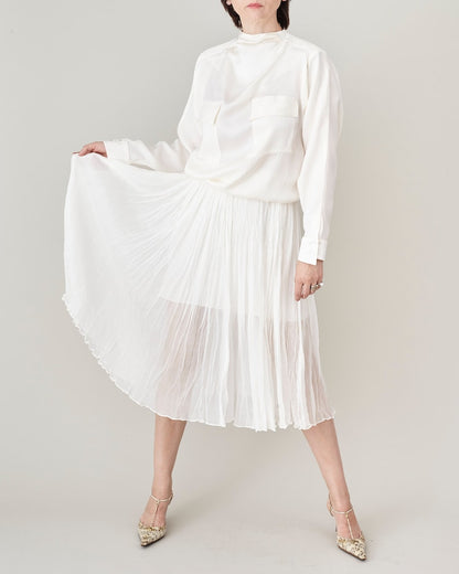 Person wearing a white micro pleated silk chiffon skirt and blouse on a plain background.