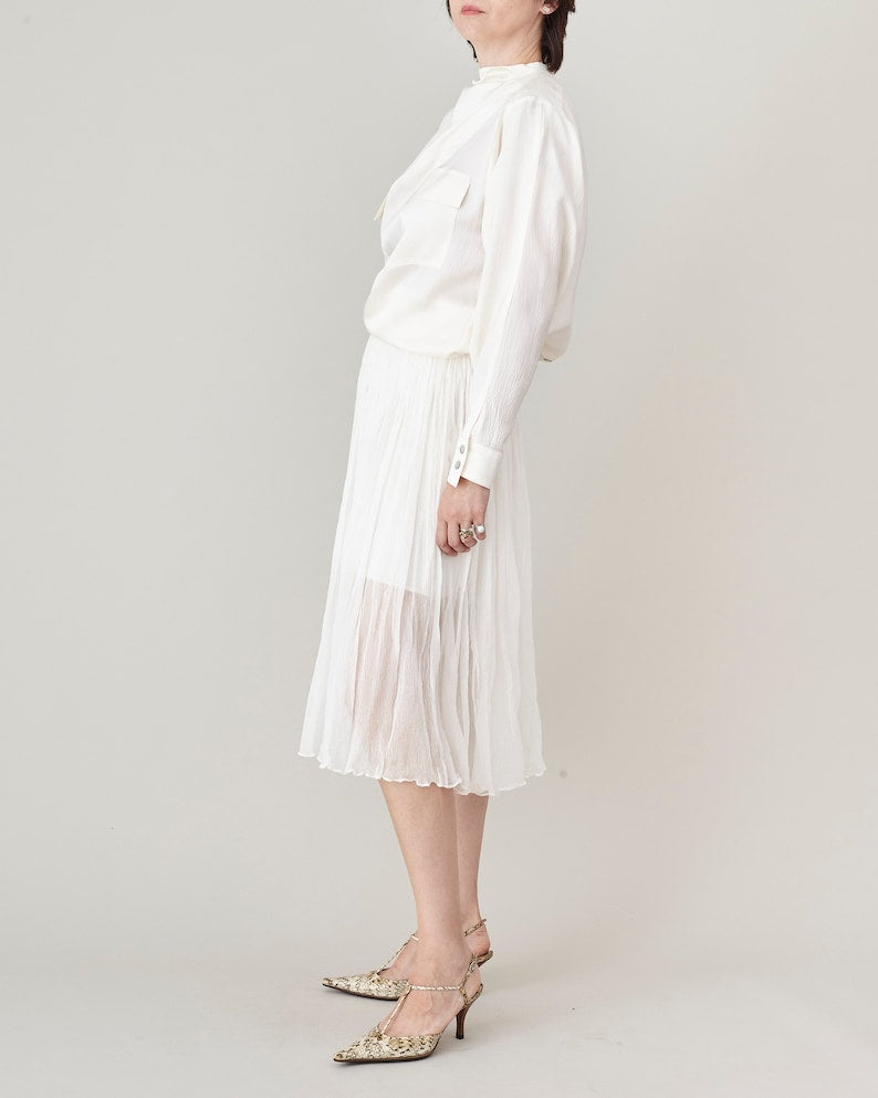 Woman wearing a all white outfit with blouse and sheer midi skirt on a plain background