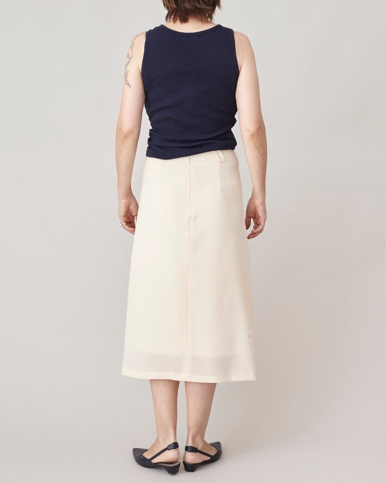 Person wearing a navy sleeveless top and cream skirt on a plain background