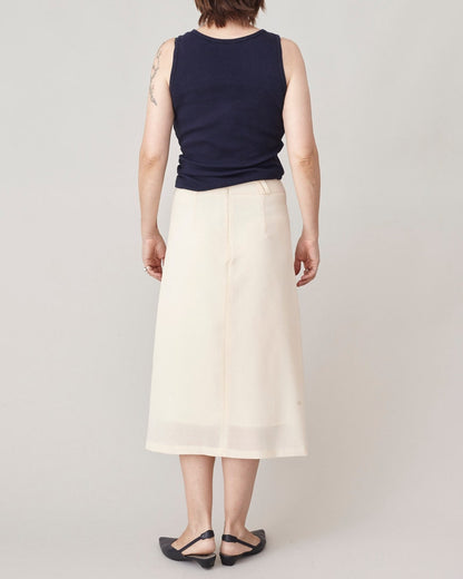 Person wearing a navy sleeveless top and cream skirt on a plain background