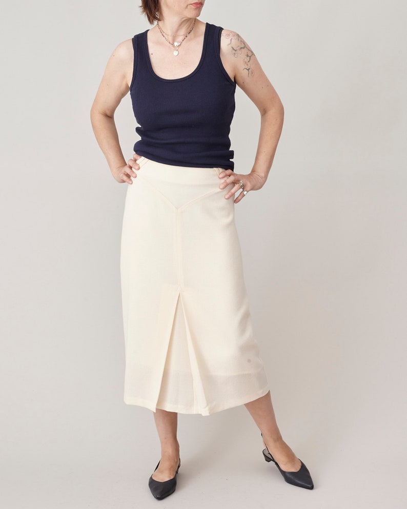 Person wearing a navy tank top and cream skirt on a plain background