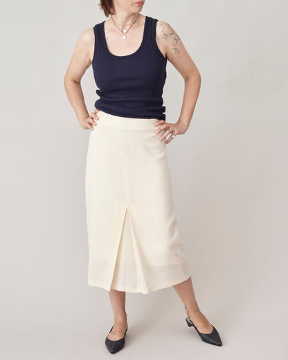 Person wearing a navy tank top and cream skirt on a plain background