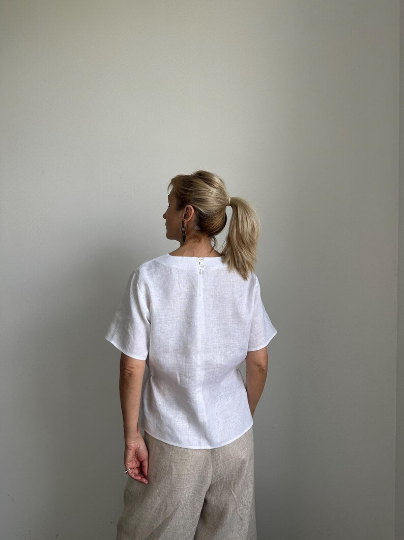 Woman wearing a white top and beige pants against a plain wall